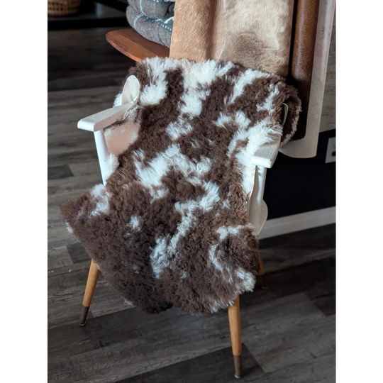 Brown and white tibet highland spotted sheepskin throw draped over a white wooden chair for cozy decor