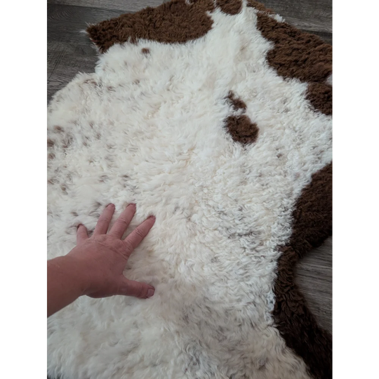 A plush white and brown tibet highland spotted sheepskin rug with soft curly texture measuring 39 by 25 inches