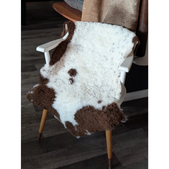 A plush white and brown tibet highland spotted sheepskin rug draped over a white wooden chair with fluffy texture