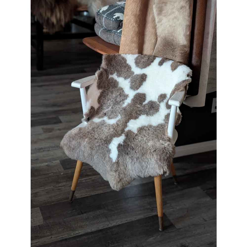 A cozy tibet highland spotted sheepskin throw in natural brown and white draped over a minimalist wooden chair