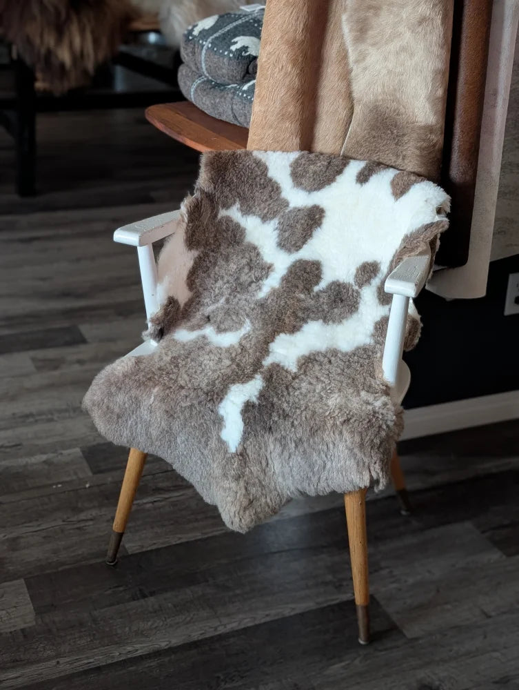 A cozy tibet highland spotted sheepskin throw in natural brown and white draped over a minimalist wooden chair