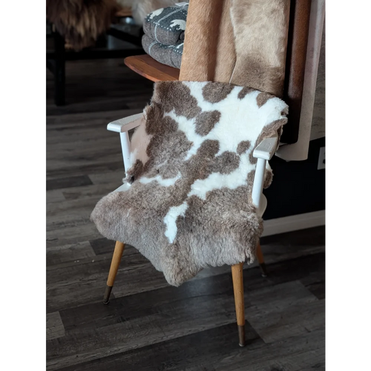A cozy tibet highland spotted sheepskin throw in natural brown and white draped over a minimalist wooden chair