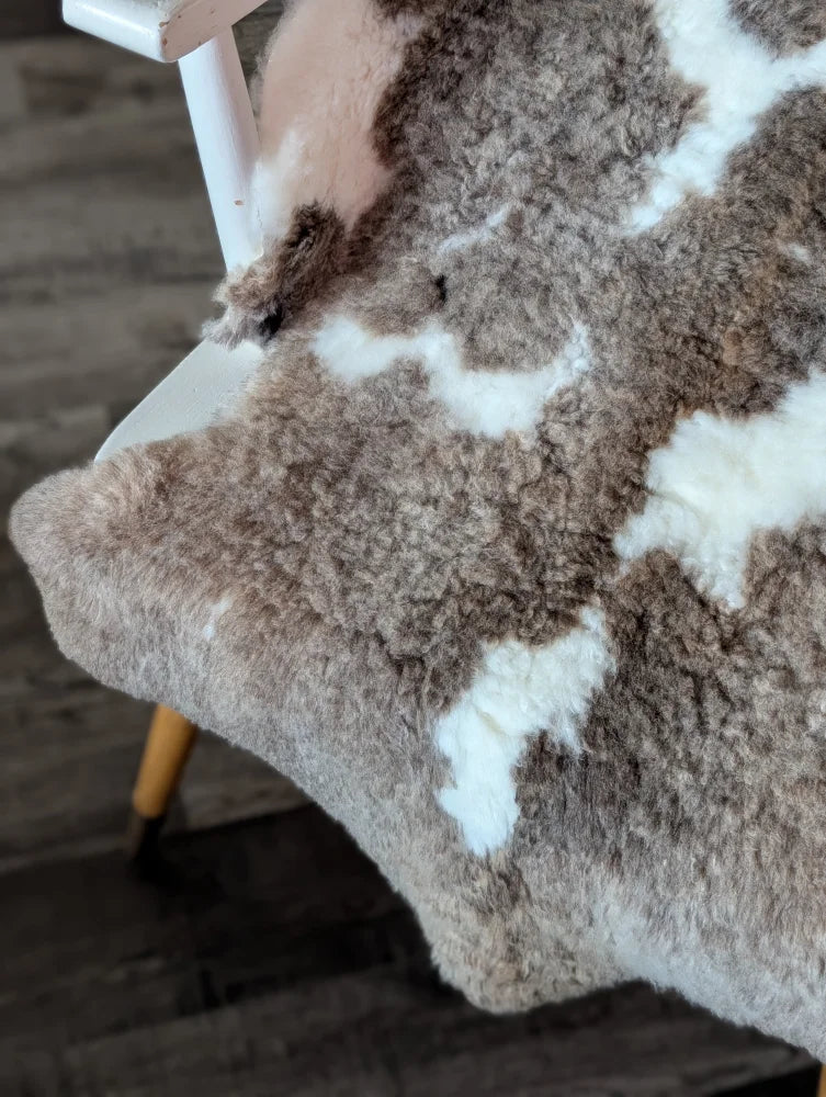A cozy tibet highland spotted sheepskin rug with soft brown and creamy white patchwork fur in 40 by 25 inches