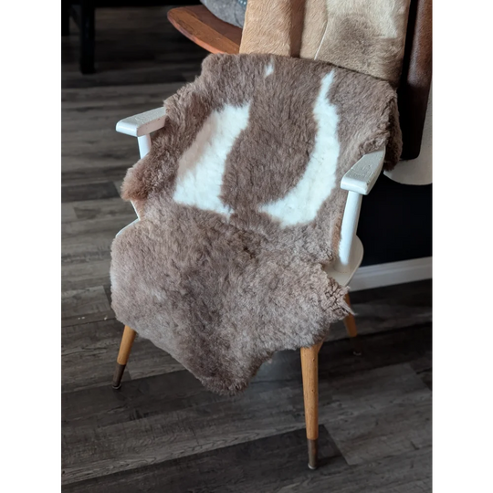 A soft natural brown and white tibet highland spotted sheepskin rug draped over the back of a wooden chair