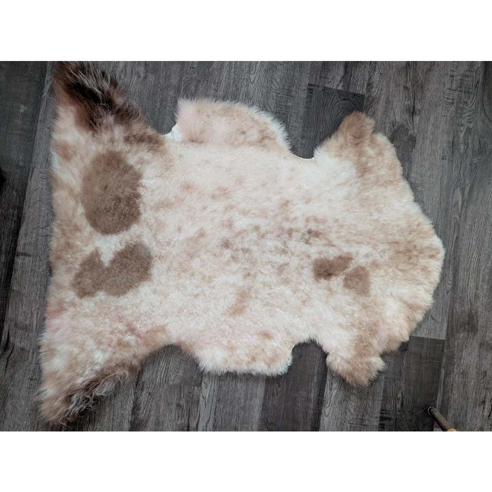 A soft cream and brown tibet highland spotted sheepskin rug with fluffy texture and organic shape 40 x 25 inches