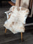 A cream and tan tibet highland spotted sheepskin rug draped over a white wooden chair with light wood legs