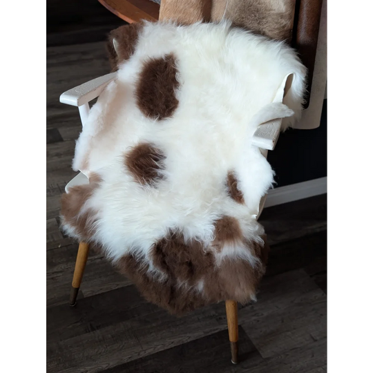 A plush white and brown tibet highland spotted sheepskin rug draped over a wooden chair showcasing its soft texture
