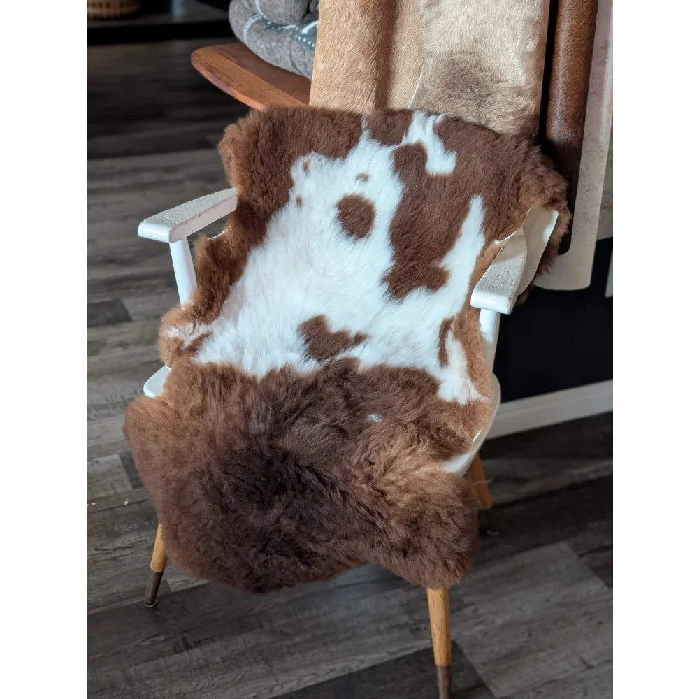 Brown and white tibet highland spotted sheepskin fur throw draped over a white wooden chair for cozy decor