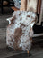 Fluffy brown and white tibet highland spotted sheepskin throw draped over wooden chair for cozy comfort