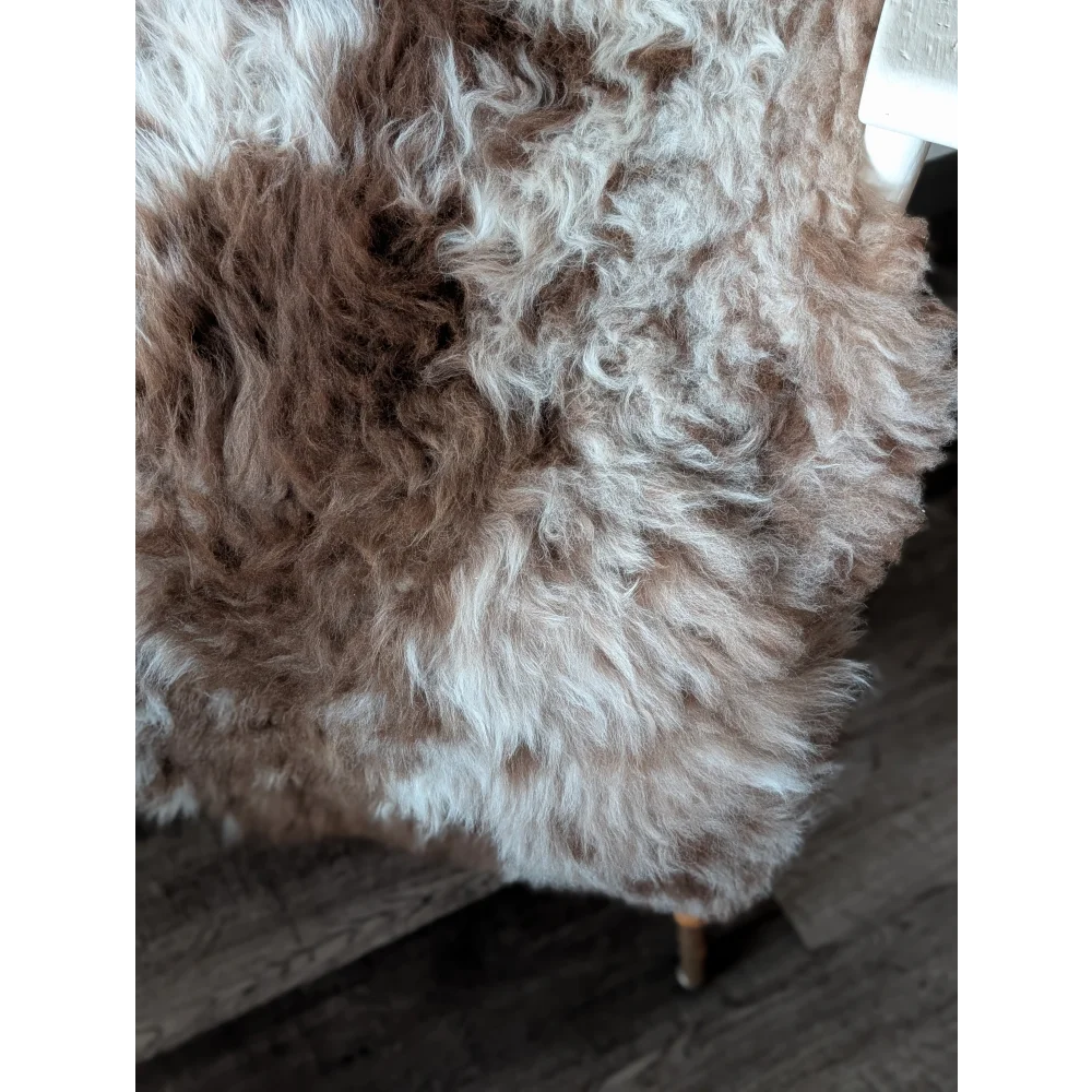 A plush curly brown and white tibet highland spotted sheepskin throw draped over a wooden chair
