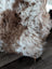 A plush curly brown and white tibet highland spotted sheepskin throw draped over a wooden chair