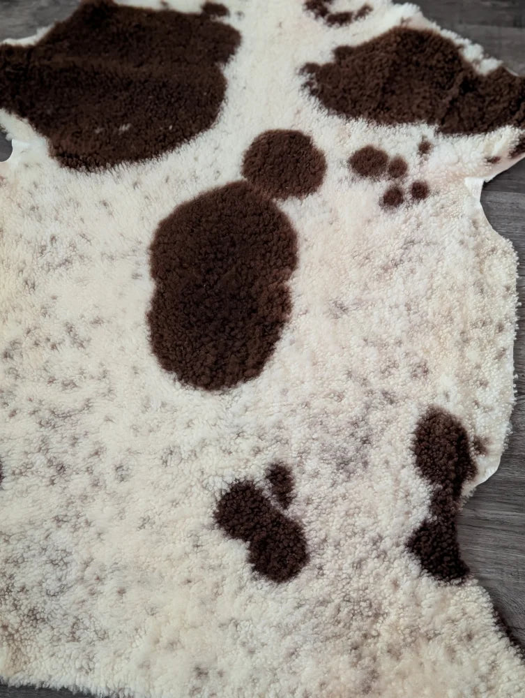 A plush cream-colored tibet highland spotted sheepskin rug with soft brown patches and fuzzy texture measuring 43.5 x 29.5 inches