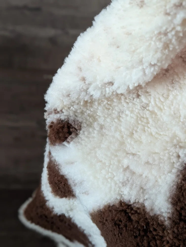 A cream and brown plush fleece blanket with a soft texture featuring a highland spotted sheepskin pattern