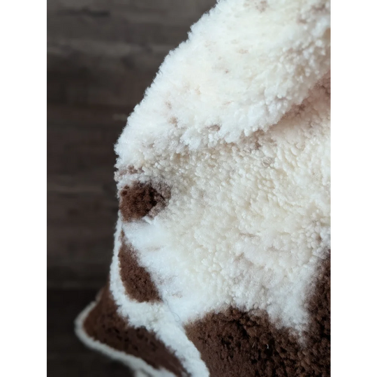 A cream and brown plush fleece blanket with a soft texture featuring a highland spotted sheepskin pattern