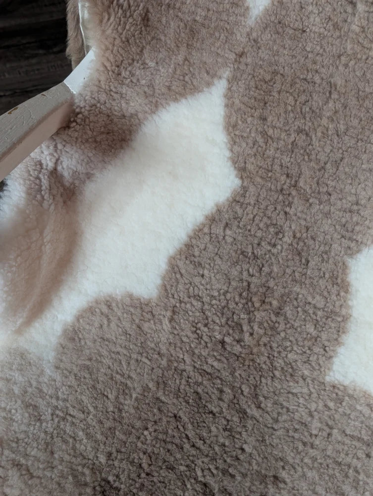 A cozy plush beige and white teddy bear style blanket made of grade a tibet highland spotted sheepskin measuring 41 x 25.5 inches