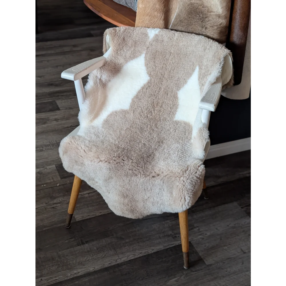 A cozy cream and white tibet highland spotted sheepskin blanket draped over a white chair with light wood legs