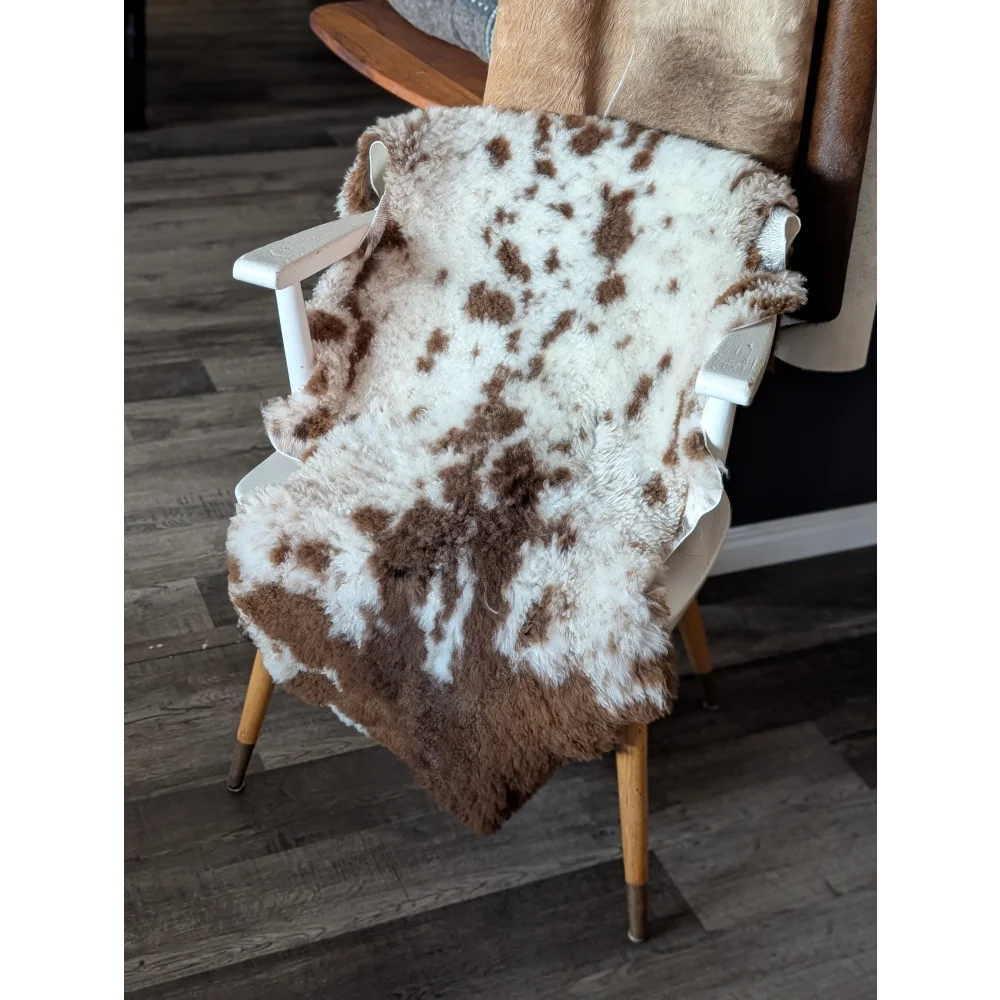 A plush white and brown tibet highland spotted sheepskin rug draped over a vintage wooden chair with fluffy texture