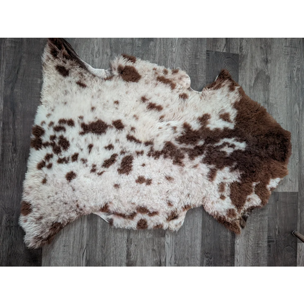 A plush tibet highland spotted sheepskin rug with brown and white spots and a soft, fluffy texture measuring 42.5 by 26 inches