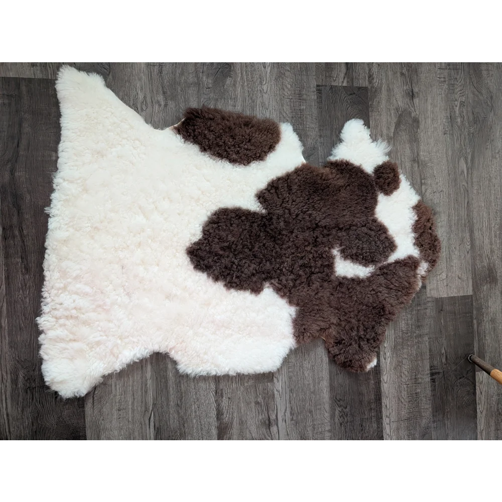 A plush irregular tibet highland spotted sheepskin rug in natural white and brown cow print measuring 41 by 25 inches