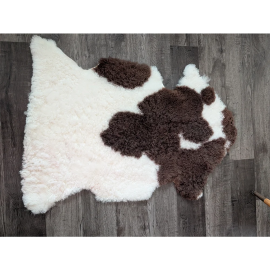 A plush irregular tibet highland spotted sheepskin rug in natural white and brown cow print measuring 41 by 25 inches
