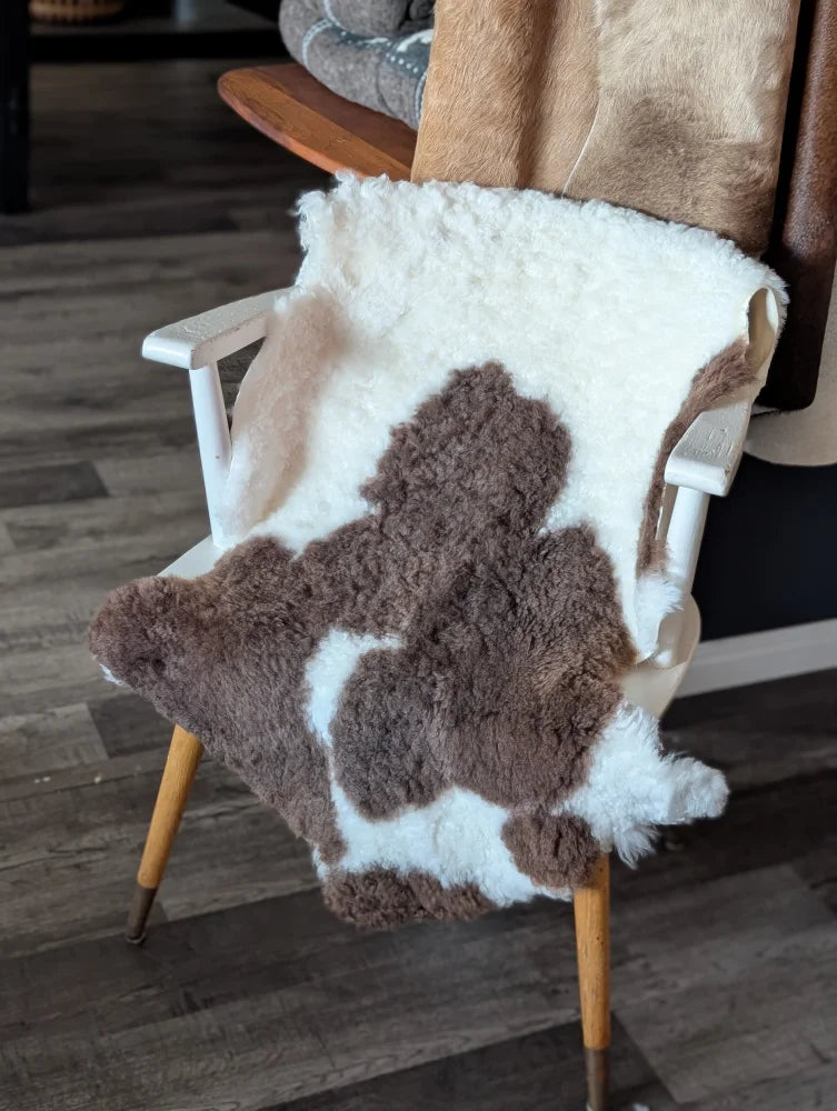 Brown and white highland spotted sheepskin throw draped over wooden chair made from tibet highland spotted wool