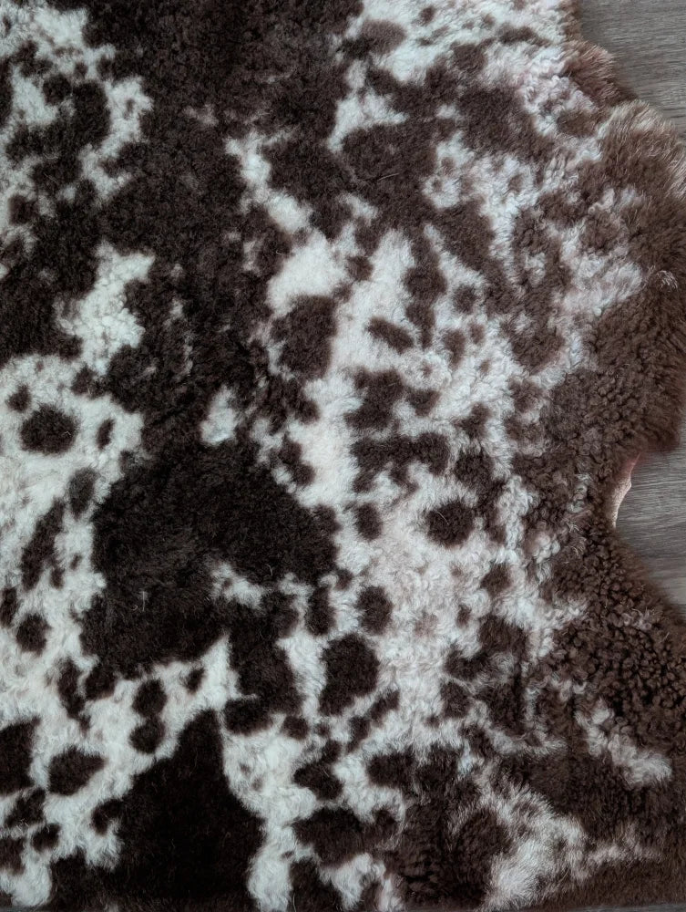 A plush tibet highland spotted sheepskin rug with natural brown and white patterns in an irregular shape