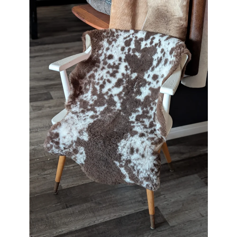 Brown and white tibet highland spotted sheepskin throw draped over a white wooden chair for cozy decor