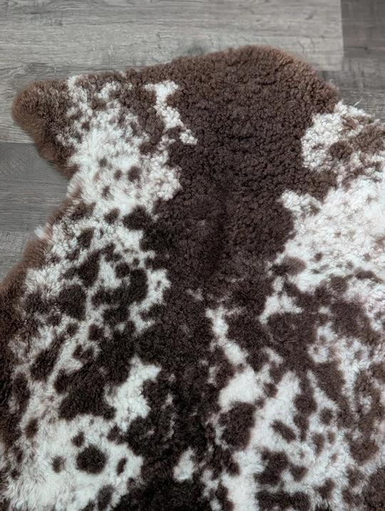 A plush tibet highland spotted sheepskin rug in brown and white with a soft fluffy texture measuring 40 by 25 inches