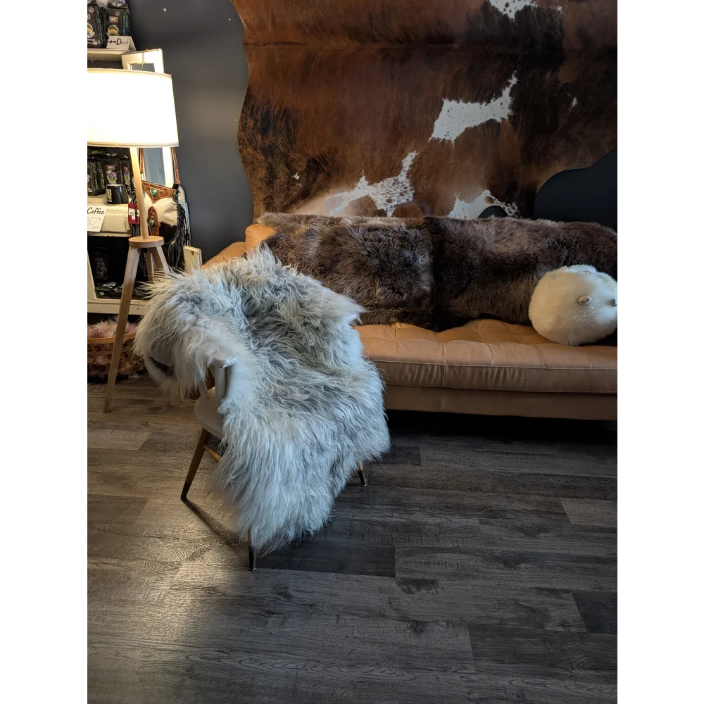 A plush light gray icelandic sheepskin throw draped over a modern chair with slender wooden legs
