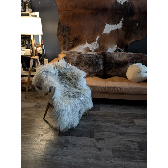 A plush light gray icelandic sheepskin throw draped over a modern chair with slender wooden legs
