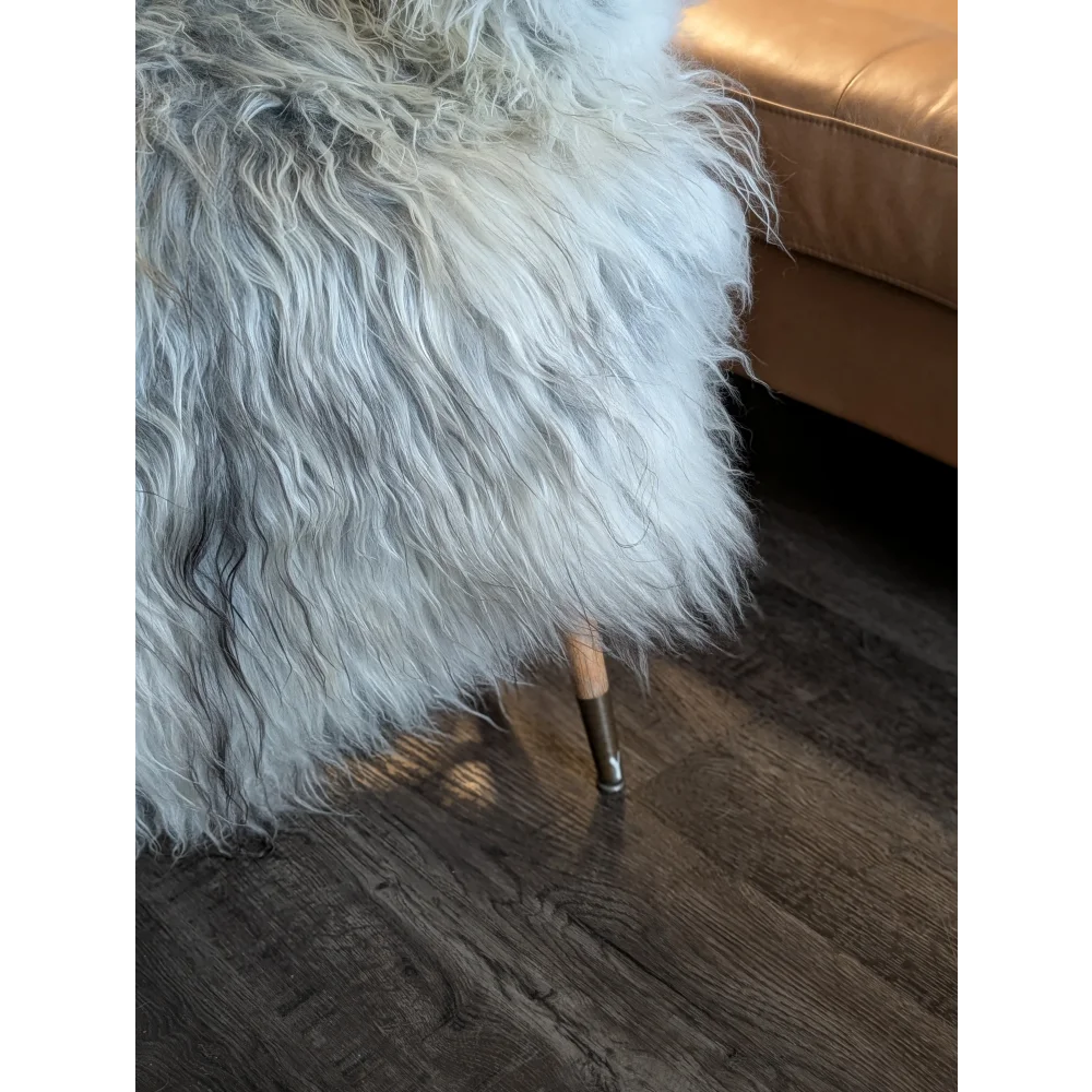 A plush long wool icelandic sheepskin throw in natural grey draped over a wooden-legged stool