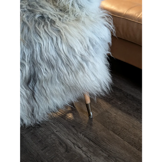 A plush long wool icelandic sheepskin throw in natural grey draped over a wooden-legged stool