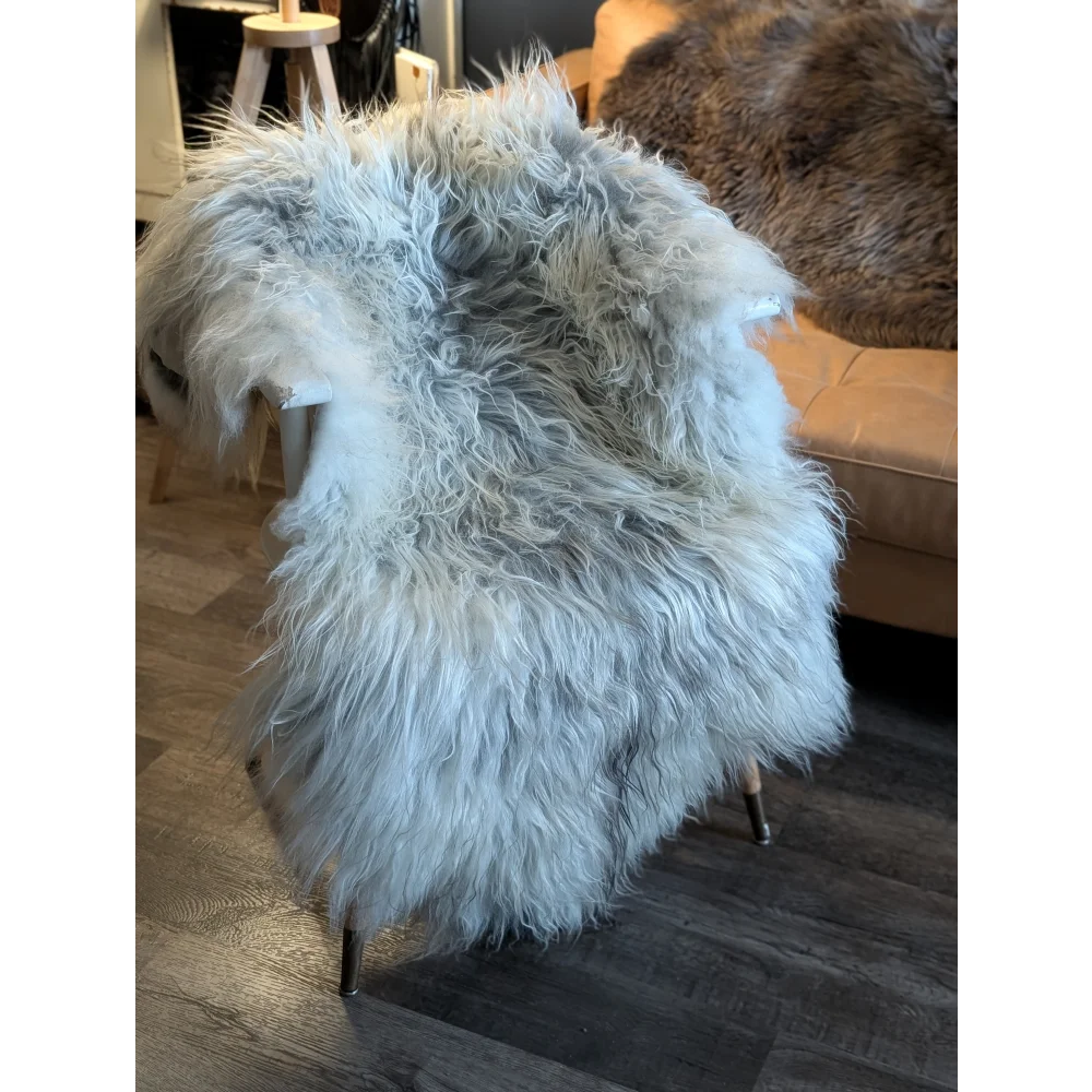 A plush light gray long wool icelandic sheepskin rug with fluffy fibers draped over a chair for cozy use