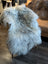 A plush light gray long wool icelandic sheepskin rug with fluffy fibers draped over a chair for cozy use