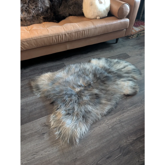 A plush naturally colored wool icelandic sheepskin rug with soft fluffy texture and irregular edges on the floor