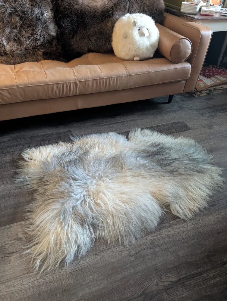 A fluffy cream-colored icelandic sheepskin rug with long soft fibers on a wooden floor for cozy decor