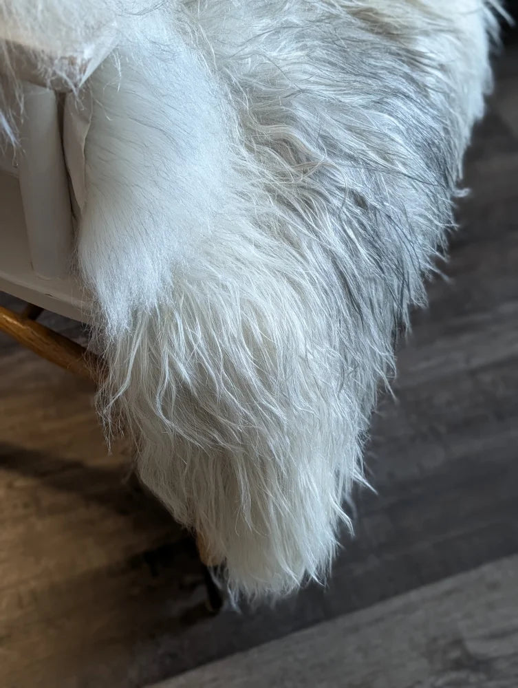 A plush long-haired white wool icelandic faux fur throw draped over furniture edge for cozy style