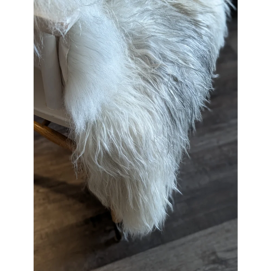 A plush long-haired white wool icelandic faux fur throw draped over furniture edge for cozy style