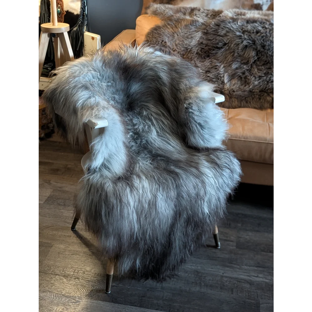 A massive 54 x 34 inch icelandic sheepskin throw in natural grey draped over a modern chair with light wood legs