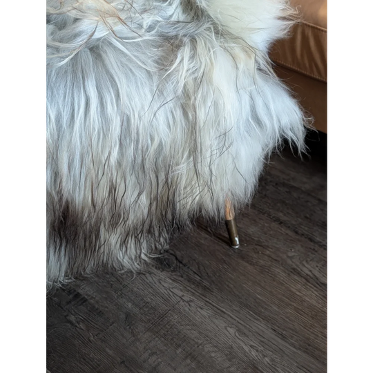 A plush white and gray faux fur ottoman with a single metallic leg made from double icelandic wool sheepskin