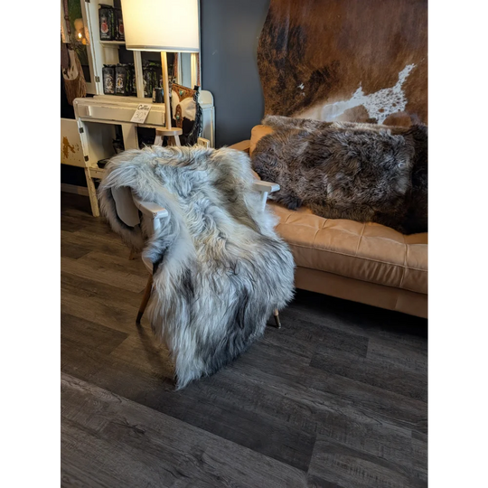 A plush wool icelandic sheepskin throw in natural grey draped over a wooden chair, measuring 58 by 32 inches