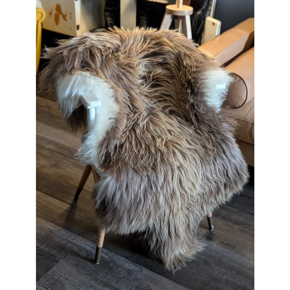 A plush long wool icelandic faux fur throw in beige and white drapes over a white wooden chair for cozy style