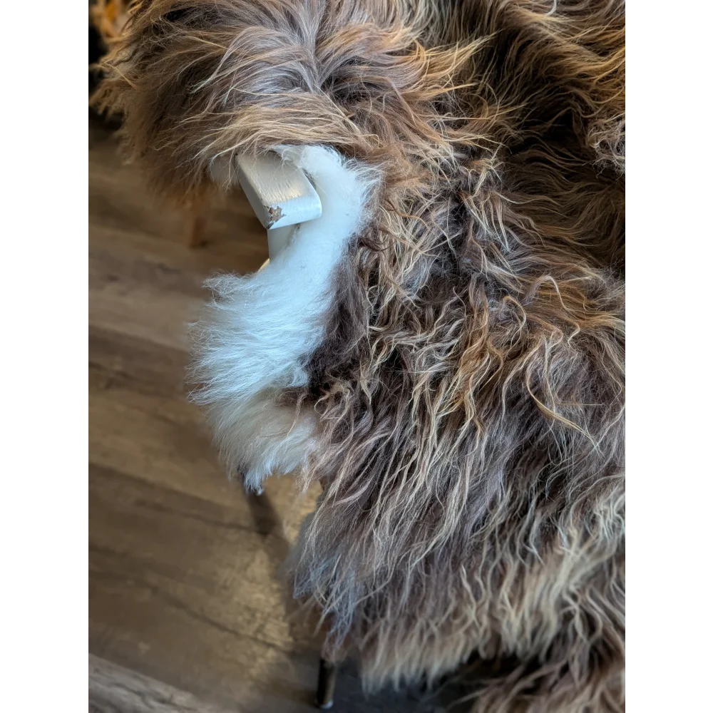 A plush shaggy brown and white wool icelandic throw draped over a white wooden chair leg for cozy decor