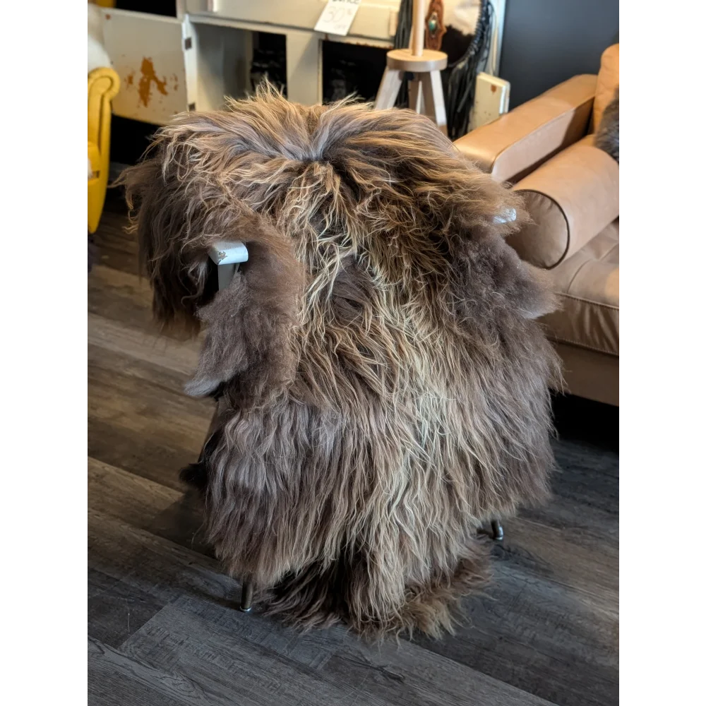 A plush shaggy long wool icelandic sheepskin throw in natural bronze draped over a modern metal stool