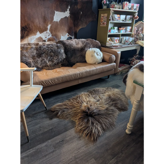 Tan leather sofa with thick shaggy brown and gray fur pillows plus a fluffy white sheep pillow and long wool icelandic sheepskin
