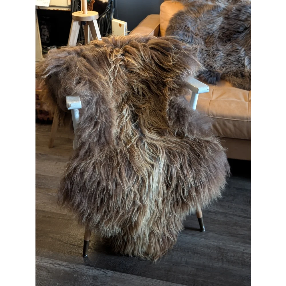 A thick shaggy long wool icelandic sheepskin rug in natural bronze draped over a white wooden chair