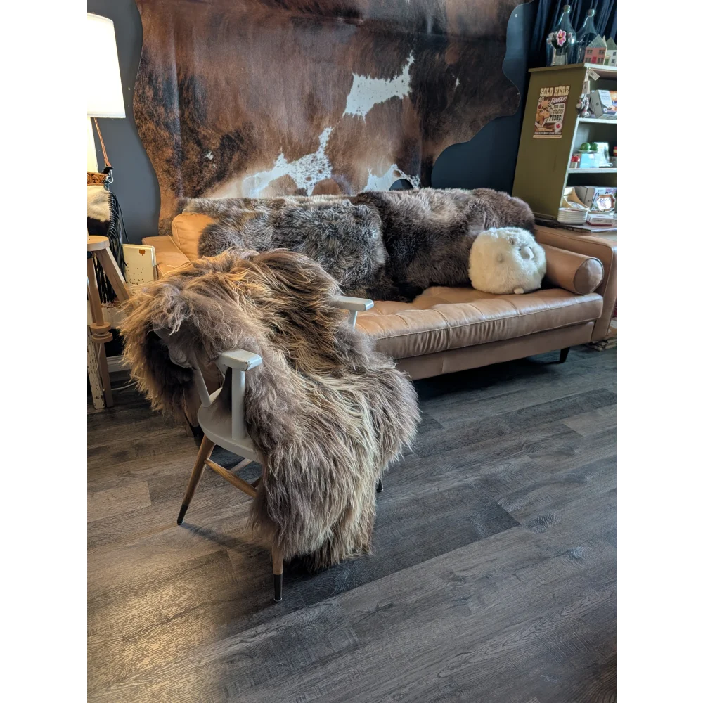Tan leather sofa draped with thick, shaggy brown and gray long wool icelandic sheepskin rugs natural bronze color