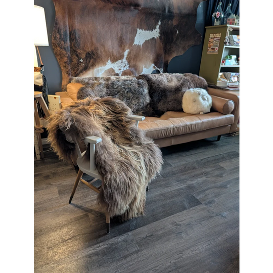 Tan leather sofa draped with thick, shaggy brown and gray long wool icelandic sheepskin rugs natural bronze color