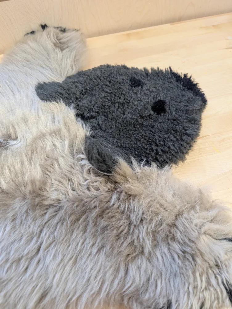 Gray plush sheep-shaped toy with black embroidered eyes on fluffy white merino sheepskin in hand made sheepskin bear rug
