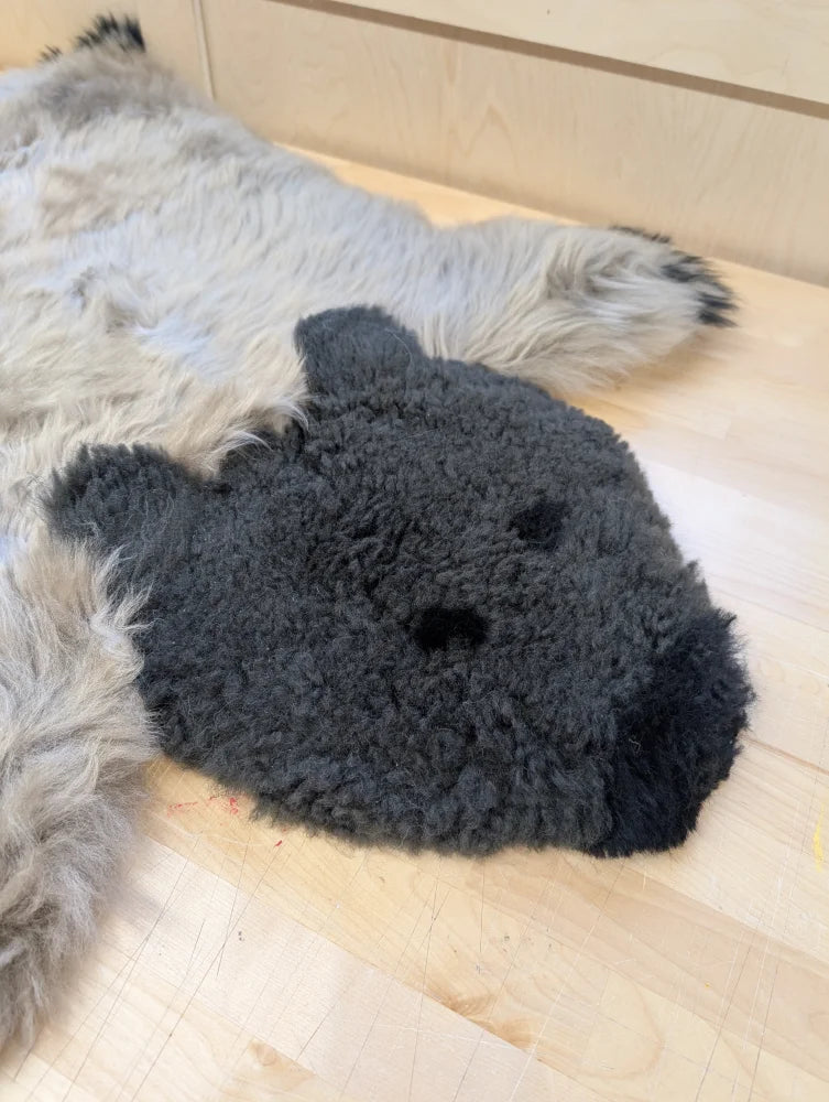 A hand made dark gray sheepskin bear rug with soft fuzzy texture and black embroidered eyes perfect as a grizzly bear rug